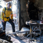 A damage inspector stands in the entryway to a burned structure in the Eaton Fire area.