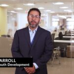 Youth Development Director David Carroll wearing blue dress shirt, black suit jacket, glasses and office in background