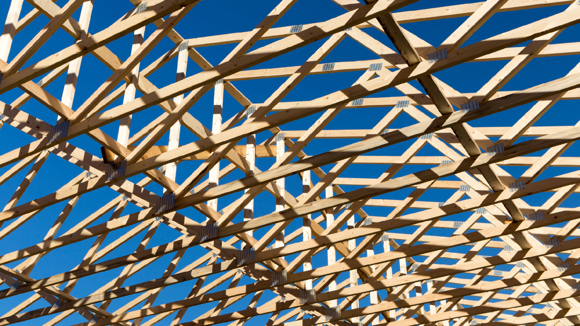 Wood framed for a roof in a repeated pattern against a blue sky.