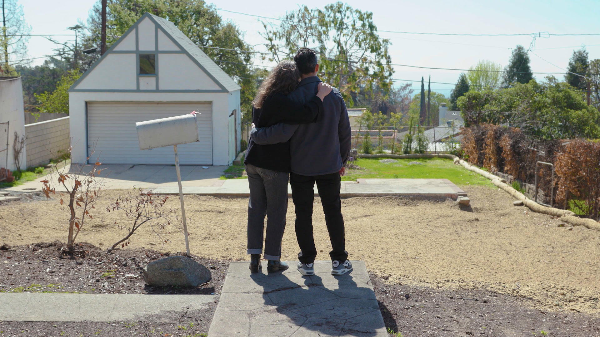 Juan and Sana face their cleared property and embrace.