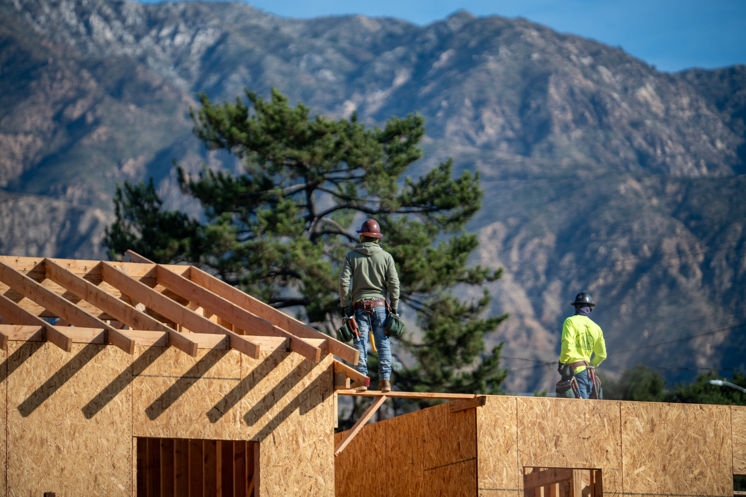 workers stand on the roof a new home under construction in Altadena with the mountains in the background.