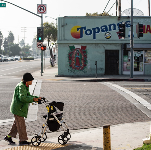 Older woman holding on a walker at the corner of an intersection with a building to the background and street light